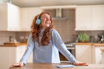 Joyful Woman With Curly Red Hair Enjoying Music While Cooking in Modern Kitchen