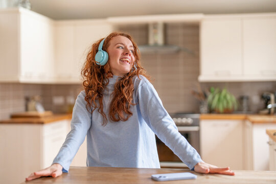 Joyful Woman With Curly Red Hair Enjoying Music While Cooking in Modern Kitchen
