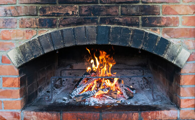 Traditional brick oven for cooking and baking food. Firewood burns in the oven. Wood-burning stove. Image of a brick pizza oven with fire. Flames and fire from burning wood