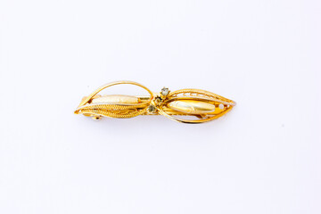 A golden colored brooch shaped like a leaves. A brooch is a piece of jewelry that serves both functional and decorative purposes. This photo is taken from the front.