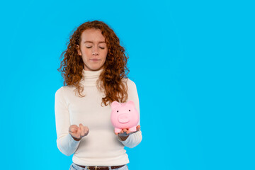 Young Woman Contemplating Savings While Holding Pink Piggy Bank Against Bright Blue Background