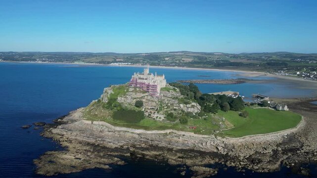 St Michael's Mount, Cornwall, England: DRONE VIEWS: St Michael's Mount with the coastline looking towards Penzance in the background; a causeway links the island to Marazion at low tide (Clip 6).