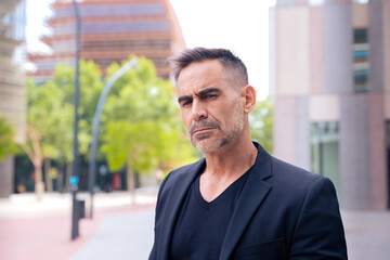 Obraz premium Close-up of a caucasian businessman looking angry at the camera in a suit standing in outdoor workspace. Front view of a young lawyer with thoughtful expression staring