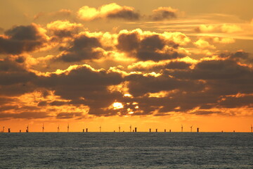 Sunset offshore in the North Sea with wind farm and vessels in front of it.