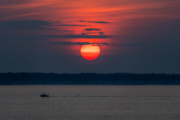 The sun is enormous and pink during a sunset over the water of the Assawoman bay in Ocean City, Maryland.