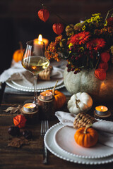 Elegant atmospheric beautiful dinner table setting for thanksgiving or wedding celebration, fall countryside style, pumpkins as decor. Romantic cozy home atmosphere. Wine, floral pumpkin centrepiece.