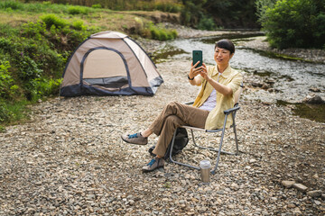 japanese woman sit in front of tent and have a video call on cellphone