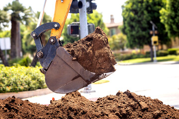 Close up of a backhoe scoop bucket filled with dirt . The work is being done at a residential intersection.