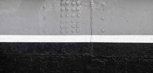 Riveted side of the warship painted in gray and black with white waterline as an industrial background
