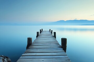 Fototapeta premium Wooden pier extending into calm blue water on a foggy morning