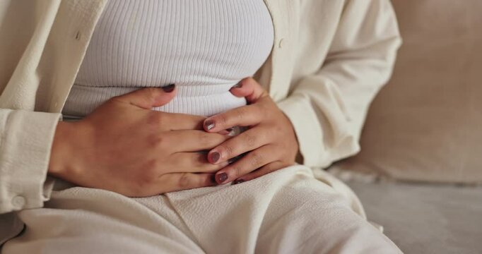 Tummy cramps, hands and woman on sofa in home with menstruation, periods or constipation. Stomach pain, sick and closeup of female person rubbing belly for IBS, endometriosis or virus in living room.