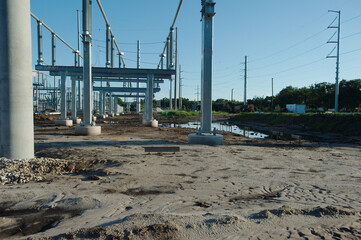 Wide view of  Electric substation under construction. Dirt piles from construction and equipment tire tracks with High Power Lines in Florida. Blue sky.  Upgrading infrastructure with large metal pole