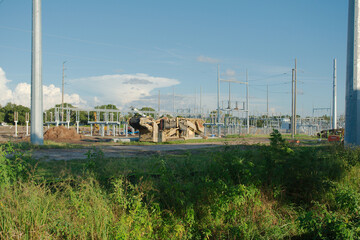 Obraz premium Wide view of Electric substation under construction. Dirt piles from construction and equipment tire tracks with High Power Lines in Florida. Blue sky. Upgrading infrastructure with large metal pole