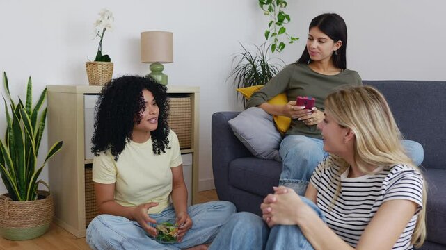Young group of female friends having fun telling stories at home, spending time together. Millennial friends talking while having lunch in the living room. Domestic life style and friendship concept