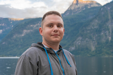 A 25-30 year old man stands by a lake surrounded by mountains, enjoying the peaceful scenery in a natural setting.