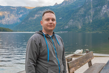 A 25-30 year old man stands at a wooden pier near a quiet mountain lake,