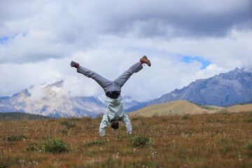 Woman hiker doing a handstand on high altitude mountain meadow