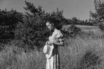 Woman standing in tall grass in long dress for fashion and beauty photoshoot in black and white...
