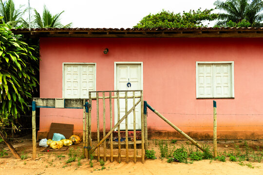 pink simple house with white doors and windows,  with a little trash in the corner and a simple gate on the entry in a street without paving