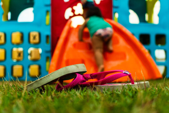 baby girl playing on a orange slider on a blue playground for children with a beautiful light. her pink little sandals are upside down on the green  grass