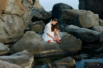 Serene woman in white dress sitting peacefully on solitary rock amidst vast ocean