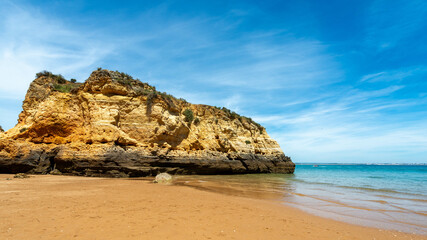  A pristine golden sand beach with a towering cliff under a vibrant blue sky in the Algarve, Portugal.