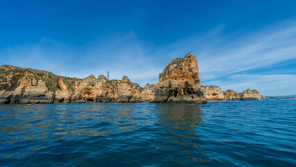 Scenic view of the Algarve coastline's rock formations at sunrise, with calm blue waters and a clear sky, Portugal.