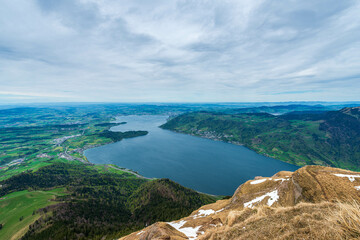 Fototapeta premium A Swiss Alps vista reveals a stunning panoramic view of Lake Lucerne nestled amidst rolling green hills, framed by a dramatic sky with swirling clouds.