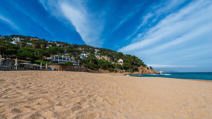 Picturesque Mediterranean beach with golden sand, turquoise water, and coastal hillside.