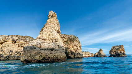 Dramatic limestone sea stacks rise majestically from the turquoise waters of the Algarve coastline in Portugal, creating a stunning seascape under a vibrant blue sky.