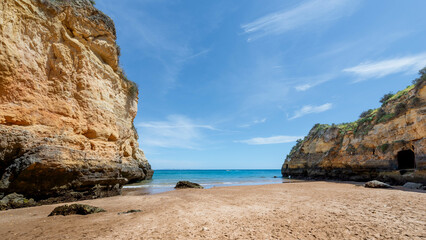 Scenic Algarve beach with golden sand, turquoise water and towering cliffs under blue sky.