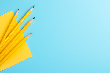Four yellow pencils resting on a vibrant blue background with a yellow notepad