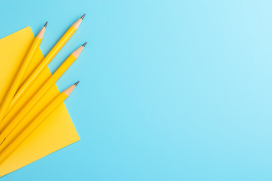 Four yellow pencils resting on a vibrant blue background with a yellow notepad