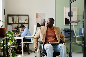 Person in wheelchair working at desk in light-filled office next to colleague sitting at separate...