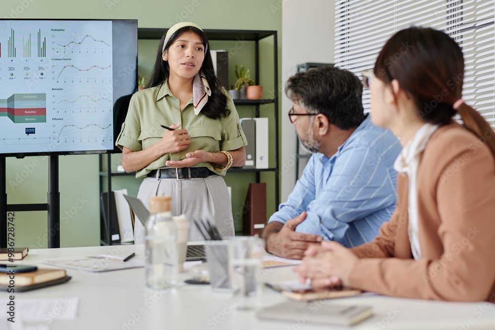 Aufkleber Presenting business strategies to professional colleagues in modern office setting with charts and graphs displayed on large screen in background. Engaging in focused discussion about data trends