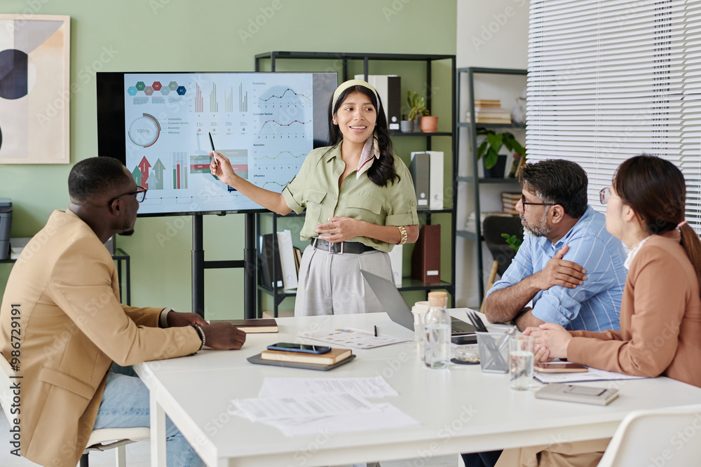 Poster Businesswoman presenting data on screen to diverse colleagues in modern office environment. Engaging in discussion while using presentation tools and charts