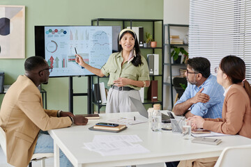 Businesswoman presenting data on screen to diverse colleagues in modern office environment....