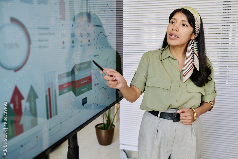 Poster woman wearing headscarf presenting data on large screen in office setting holding pointer, she is di
