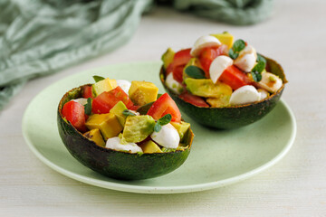 Avocado boats stuffed with mozzarella cheese, arugula and cherry tomatoes on green plate. Vegetarian Salad. Healthy food and dieting concept.