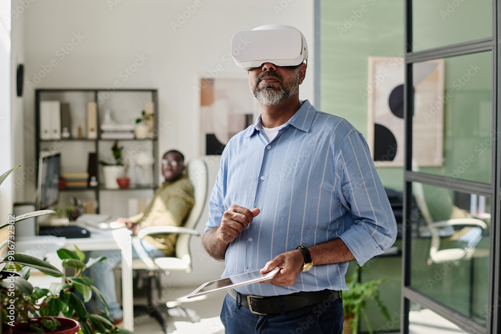 Poster man engaging with virtual reality headset in modern office setting, standing near desk with colleagu