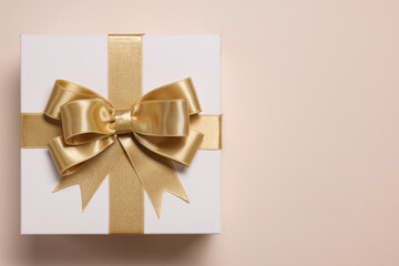 Gift box with bow on beige background, top view