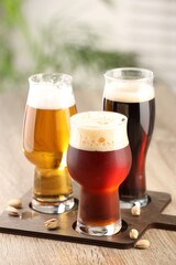 Glasses with different types of beer and pistachio nuts on wooden table indoors
