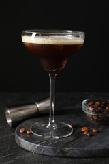 Glasses of delicious espresso martini, jigger and coffee beans on dark textured table, closeup