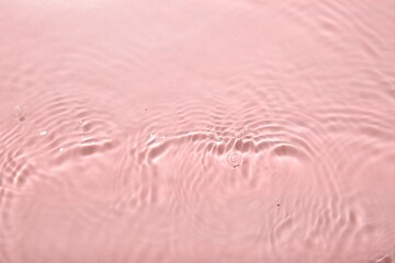 Rippled surface of clear water on pink background, top view