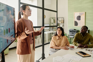 Multiracial team analyzing business data with professional presenting information in modern office conference room using technology and visual aids during daytime meeting