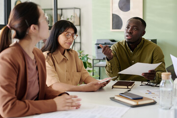 Group of diverse colleagues brainstorming ideas together, holding documents, and sharing insights during business meeting in modern office environment