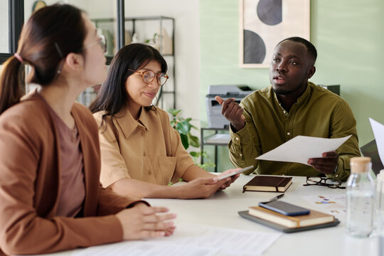 Group of diverse colleagues brainstorming ideas together, holding documents, and sharing insights during business meeting in modern office environment