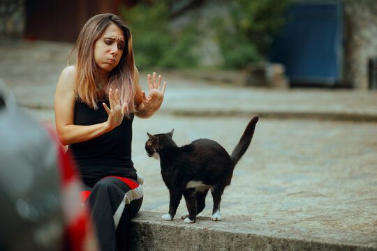 Stressed Woman Disliking a Cat That Follows Her Around. Unhappy lady saying no to a kitten waiting to be friends 

