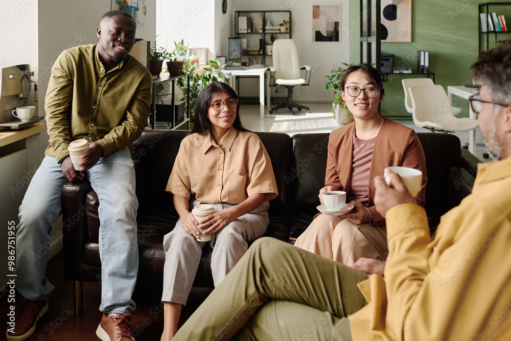 Poster group of diverse coworkers sitting on a couch and exchanging ideas in modern office with relaxed atm