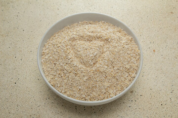 top view of whole wheat forming a heart, texture of quick oat flakes in a white bowl with a white marble bottom